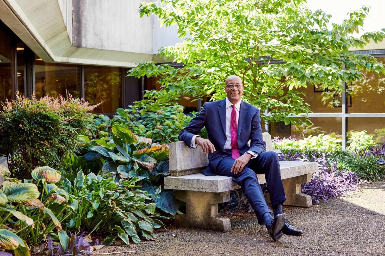 Dr. Joseph Webb, D.Sc., MSHA, FACHE, seated outdoors on a stone bench, smiling
