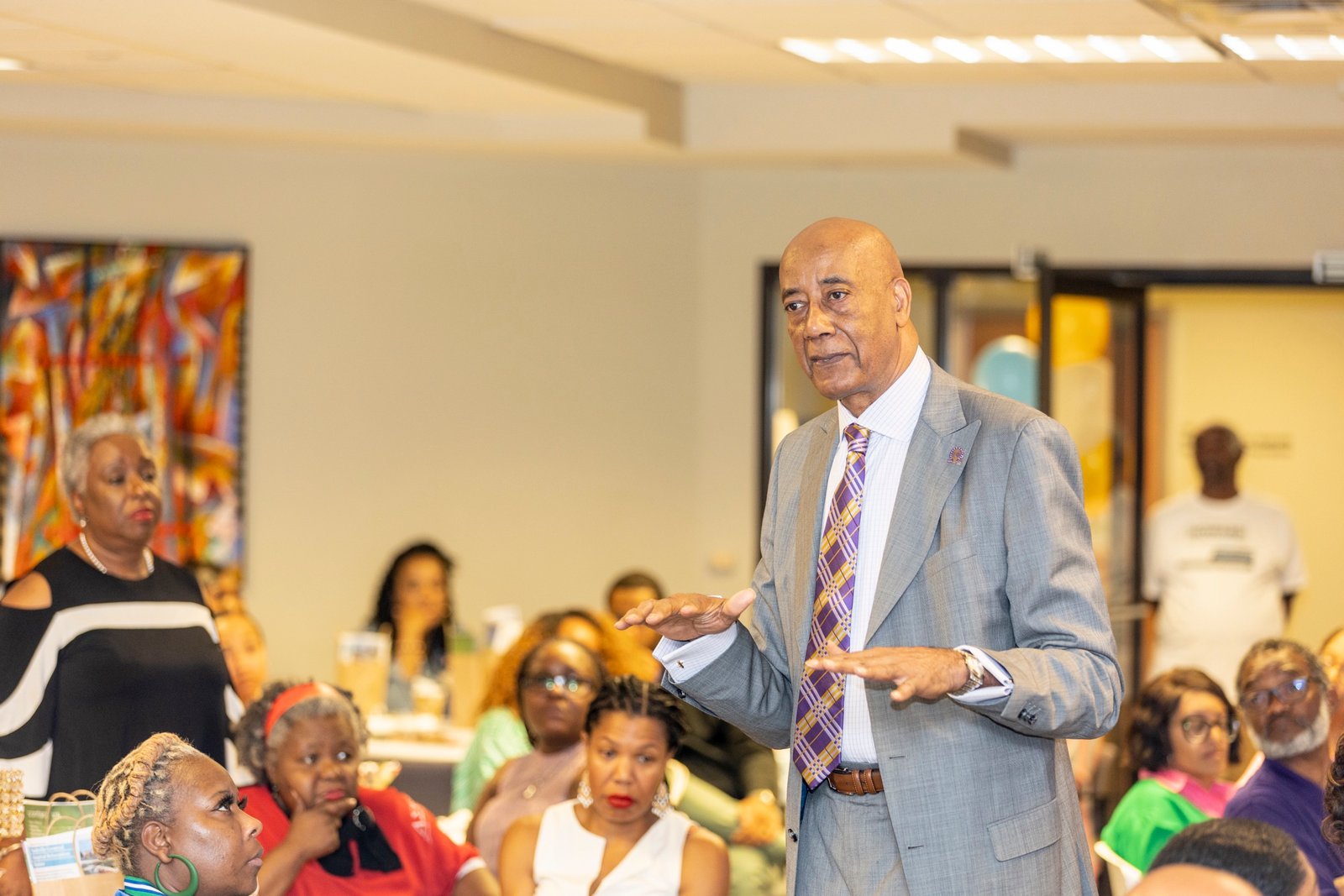 Dr. Joseph Webb speaking to a seated community audience, gesturing as he explains a point